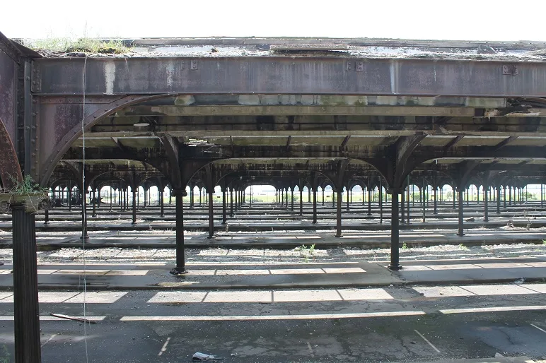 modern photograph of multiple rows of old rail lines with covered platforms, with grass growing between cracks in the concrete